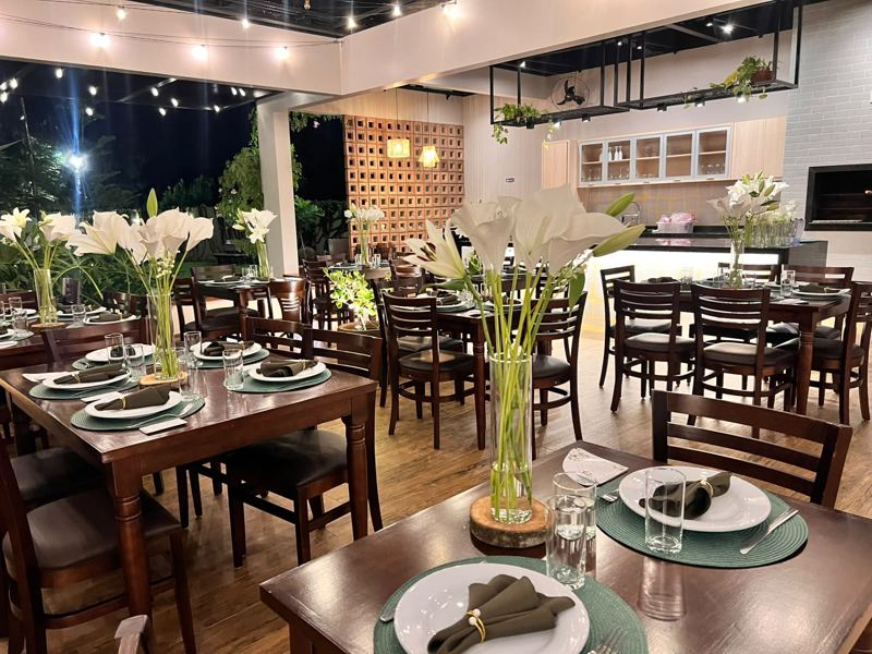 Salão do Festou à noite preparado para casamento, com mesas de madeira, lírios e luzes de varal, em Realeza PR